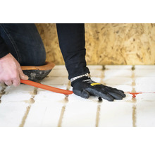 Installatie van een vloerverwarmingsbuis in een systeemplaat door een persoon met werkhandschoen.