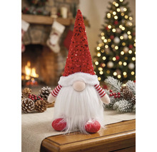 Kerstkabouter met rode lovertjesmuts en witte baard van imitatiebont op een tafel voor een warme open haard en een sfeervolle kerstboom.