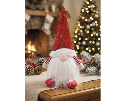 Kerstkabouter met rode lovertjesmuts en witte baard van imitatiebont op een tafel voor een warme open haard en een sfeervolle kerstboom.