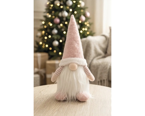 Stoffen kabouter met puntmuts en baard op een houten tafel in een lichte, feestelijk versierde kamer met een kerstboom.