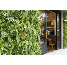 Verticale tuin met varens en kunstplanten naast een glazen café-ingang met zwart frame.