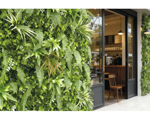 Verticale tuin met varens en kunstplanten naast een glazen café-ingang met zwart frame.
