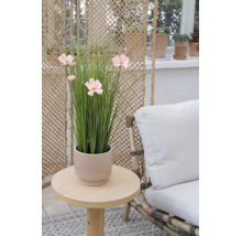 Kunstgras met roze bloemen in een geribbelde pot op een ronde houten tafel naast een fauteuil met wit kussen.