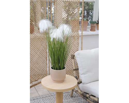 Kunstgras met witte pluimen in een geribbelde pot op een houten bijzetttafel in een lichte woonruimte.