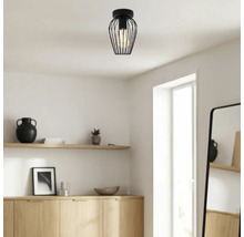 Moderne zwarte plafondlamp met draadkap in een lichte, minimalistische kamer met houten meubels.