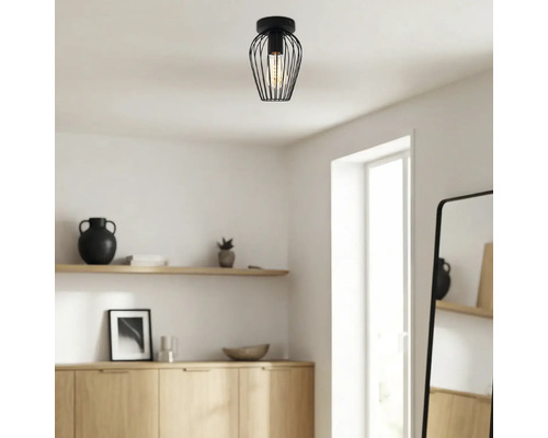 Moderne zwarte plafondlamp met draadkap in een lichte, minimalistische kamer met houten meubels.