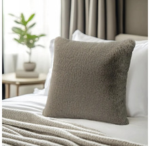 Vierkant sierkussen van imitatiebont op een bed met een gebreide deken in een lichte slaapkamer.