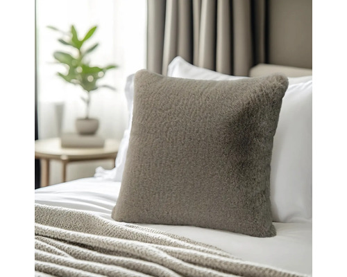 Vierkant sierkussen van imitatiebont op een bed met een gebreide deken in een lichte slaapkamer.