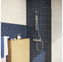 Moderne douche met verchroomde doucheset op donkerblauwe tegels, een gele betegelde wand en blauwe tegels in visgraatpatroon.