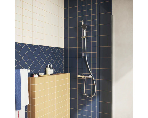 Moderne douche met verchroomde doucheset op donkerblauwe tegels, een gele betegelde wand en blauwe tegels in visgraatpatroon.