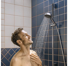 Man onder een verchroomde handdouche aan een glijstang in een badkamer met blauwe en witte tegels.