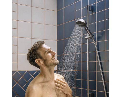 Man onder een verchroomde handdouche aan een glijstang in een badkamer met blauwe en witte tegels.