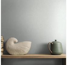 Behang met textuur en fijne linnenlook op een wand achter een houten plank met decoratieve objecten.