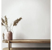Minimalistisch interieur met een houten bank en een gestructureerde vaas met gedroogd rietgras voor een lichte muur.
