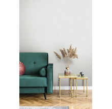 Moderne woonkamer met groene fluwelen bank en gouden bijzettafels. Een vaas met gedroogd pampasgras op tafel voor een licht gestructureerd behang.
