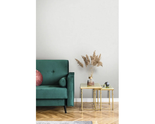 Moderne woonkamer met groene fluwelen bank en gouden bijzettafels. Een vaas met gedroogd pampasgras op tafel voor een licht gestructureerd behang.