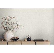Lichtbeige behang met linnenstructuur achter dressoir met decoratieve takken in een vaas en theeservies in minimalistische stijl.