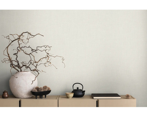 Lichtbeige behang met linnenstructuur achter dressoir met decoratieve takken in een vaas en theeservies in minimalistische stijl.