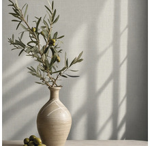 Behang met linnenlook op een muur met een keramische vaas en een olijftak in helder zonlicht.
