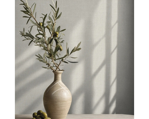 Behang met linnenlook op een muur met een keramische vaas en een olijftak in helder zonlicht.