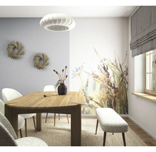 Lichte eetkamer met houten tafel, gestoffeerde stoelen en bank, een fotobehang met bloemenpatroon en een moderne hanglamp.