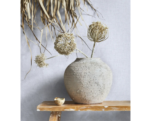 Gestructureerd behang met linnenlook op een muur achter een keramieken vaas met droogbloemen op een rustieke houten bank.