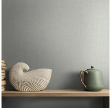 Vliesbehang met textielstructuur in linnenlook op een muur achter een houten plank met een schelpdecoratie en een theepot.