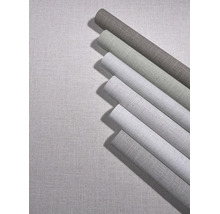 Meerdere rollen vliesbehang met linnenstructuur in verschillende tinten op een ondergrond met dezelfde textieloptiek.