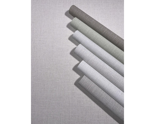 Meerdere rollen vliesbehang met linnenstructuur in verschillende tinten op een ondergrond met dezelfde textieloptiek.