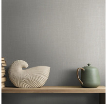 Grijs behang met linnenstructuur op een muur achter een houten plank met decoratieve schelp en theepot.