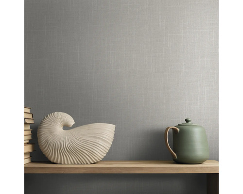 Grijs behang met linnenstructuur op een muur achter een houten plank met decoratieve schelp en theepot.