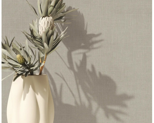 Vliesbehang met linnenstructuur in beige op een muur achter een vaas met protea-bloemen.