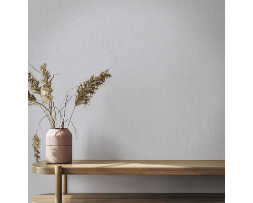 Vliesbehang met linnenlook op een muur achter een vaas met droogbloemen op een houten bank.