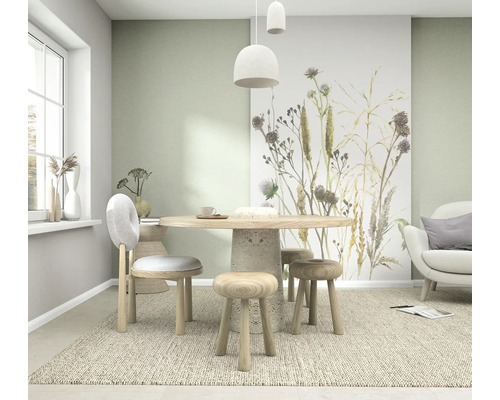 Lichte eetkamer met vliesbehang met grassen en distels, een ronde houten tafel en houten zitmeubels op een vloerkleed.