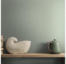 Groen vliesbehang met linnenstructuur. Interieurvoorbeeld met houten plank, witte schelpdecoratie en theepot voor een behangen muur.