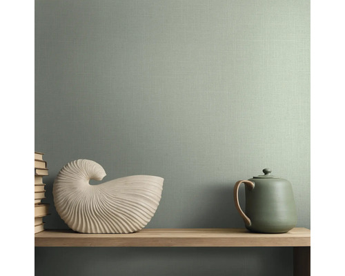 Groen vliesbehang met linnenstructuur. Interieurvoorbeeld met houten plank, witte schelpdecoratie en theepot voor een behangen muur.
