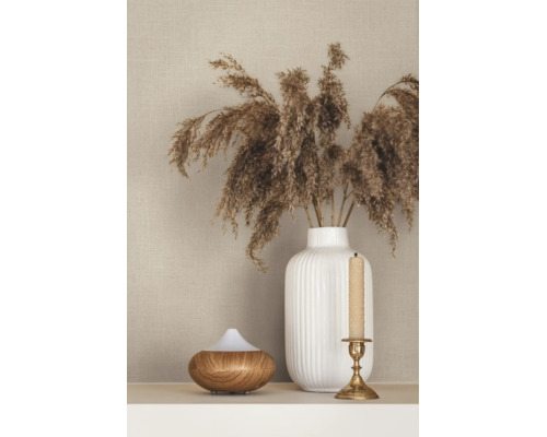 Beige behang met linnenstructuur achter een witte geribbelde vaas met drooggras, een aroma diffuser en een kandelaar.