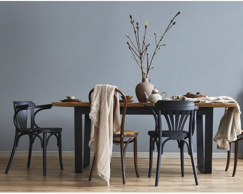 Lichte, moderne eetkamer met gestructureerd behang op de muur, een houten tafel met metalen poten en verschillende stoelen.