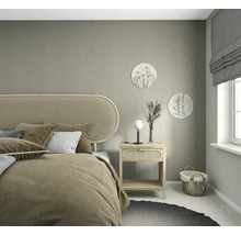 Gestructureerd vliesbehang in grijsbeige in een lichte slaapkamer met meubels van natuurlijk hout, hoofdbord van webbing en zachte decoratie.