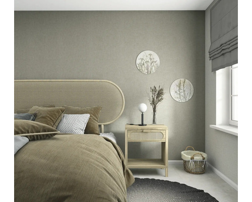 Gestructureerd vliesbehang in grijsbeige in een lichte slaapkamer met meubels van natuurlijk hout, hoofdbord van webbing en zachte decoratie.