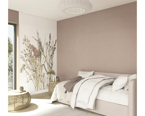 Lichte slaapkamer met wit bed, fotobehang met bloemen, een oudroze muur, bijzettafels van rotan en een ronde geplooide plafondlamp.