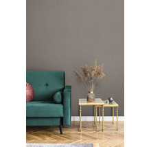 Woonkamer met gestructureerd behang met linnenlook, een groene fluwelen bank en gouden bijzettafels met droogbloemen.