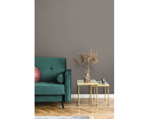 Woonkamer met gestructureerd behang met linnenlook, een groene fluwelen bank en gouden bijzettafels met droogbloemen.