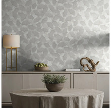 Behang met ginkgobladpatroon in een lichte, georganiseerde woonkamer met dressoir, tafellamp en decoratieve elementen.