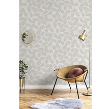 Vliesbehang met ginkgobladpatroon in een lichte woonkamer met fauteuil, vloerlamp en parketvloer.