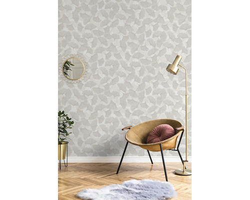 Vliesbehang met ginkgobladpatroon in een lichte woonkamer met fauteuil, vloerlamp en parketvloer.