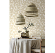 Behang met ginkgopatroon achter een ronde eettafel met linnen tafelkleed, twee gevlochten hanglampen en glazen vazen met distels.