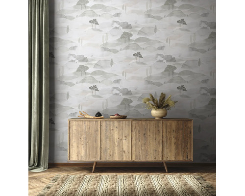 Vliesbehang met een landschapspatroon van heuvels en bomen achter een houten dressoir in een natuurlijk ingerichte kamer.