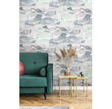 Vliesbehang met landschapspatroon in aquarel-look, heuvels en bomen in een woonkamer met groene fauteuil en bijzettafels.