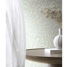 Vliesbehang met bladpatroon in een lichte kamer met houten tafel, bloemenvaas en gordijn.